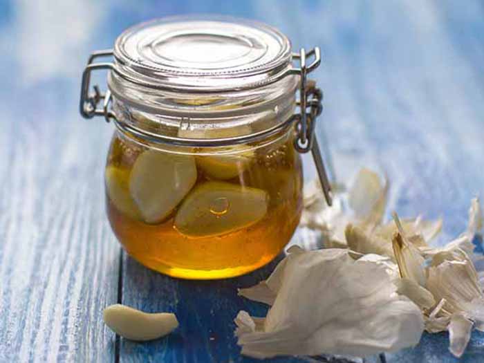 A glass container with garlic cloves in honey, and whole garlic cloves next t it