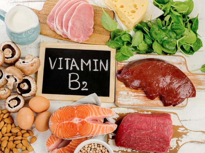 Foods rich in vitamin B2 or riboflavin (Slices of beef, pork, and fish, mushrooms, almonds, eggs, sliced cheese, spinach, and a mug of milk) on a wooden table